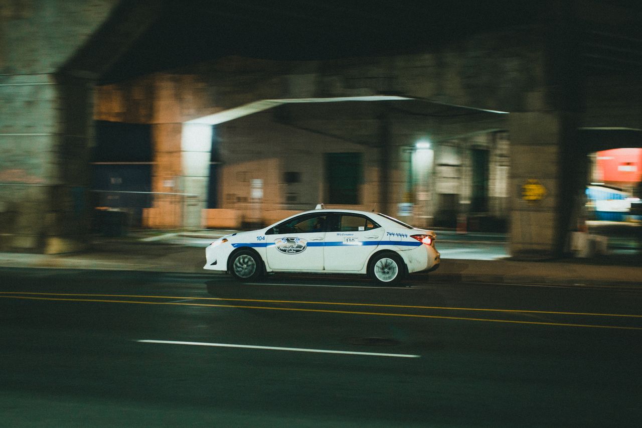 Dynamic night shot of a white taxi speeding through a city street, capturing motion.