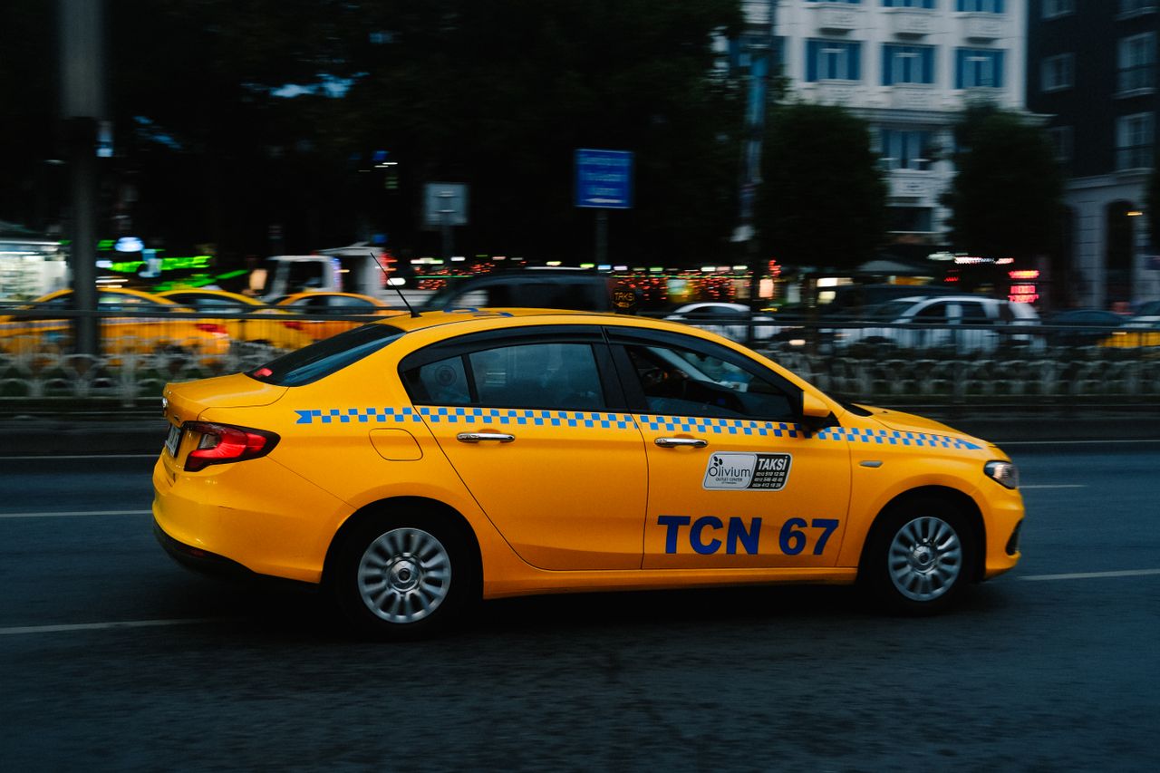 Contact A vibrant yellow taxi speeds along a bustling city street during nighttime.