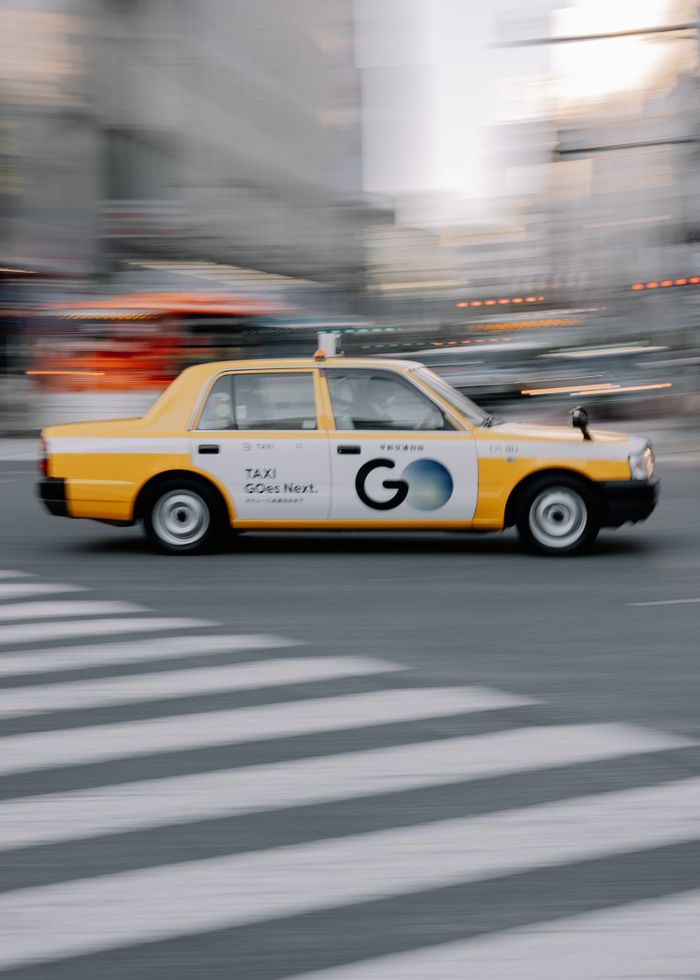 A dynamic view of a taxi speeding across a crosswalk in downtown Shibuya, Tokyo.