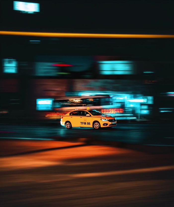 Blurred motion of a yellow taxi speeding through vibrant city streets at night.